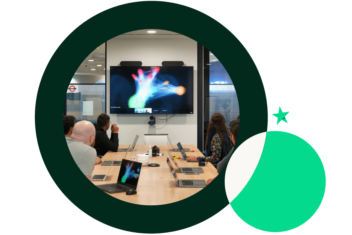 A graphic of a large dark Green circle and a smaller bright Green circle. The large circle features an image of a group of a people looking at a screen in a meeting room. The smaller circle features the Trustpilot star above it.